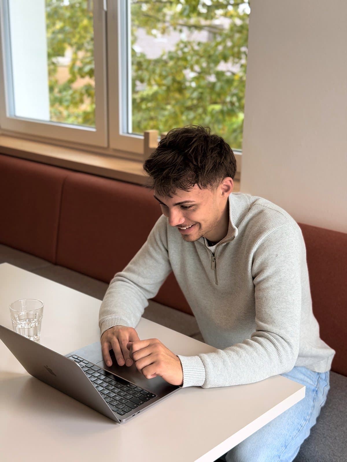 Luis Sabisch sitzt am Tisch und arbeitet am Laptop, hinter ihm ein Fenster.