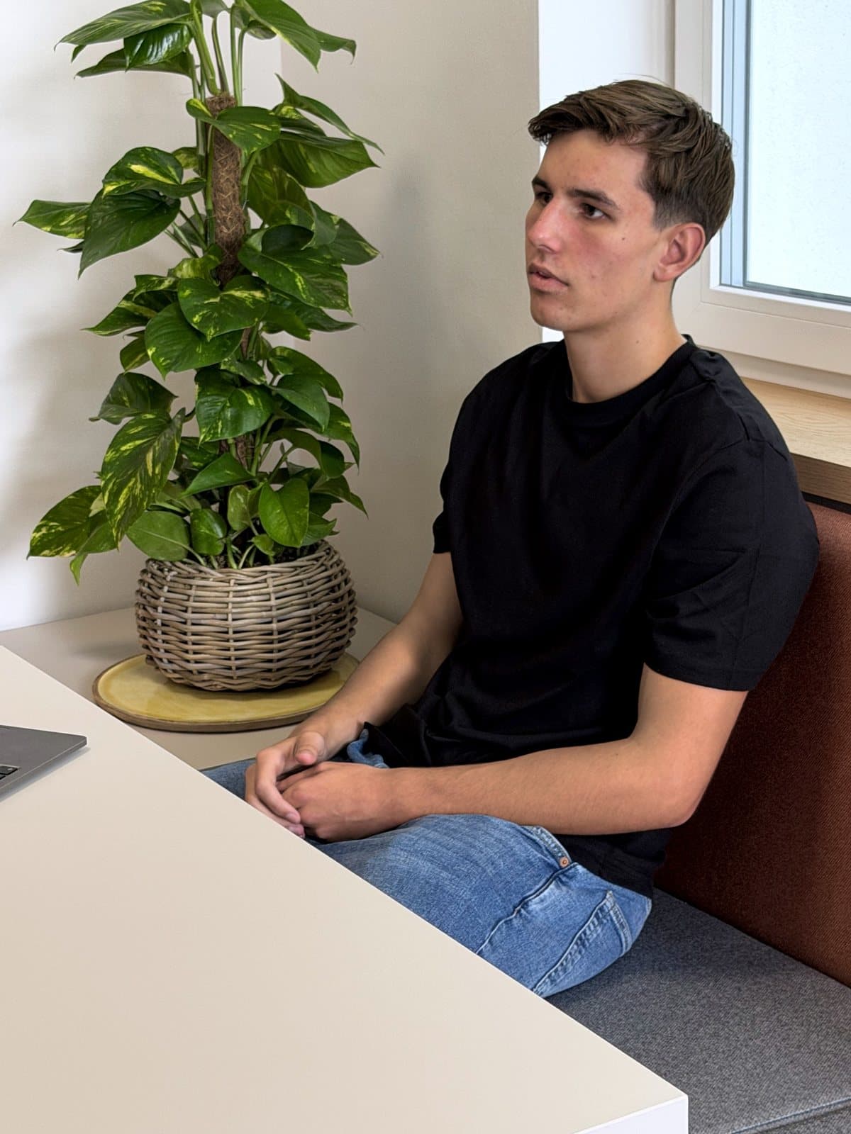Max Wiebe an der Sitzbank im Besprechungsbereich, die Hände im Schoß gefaltet, seinem Gegenüber zugewandt.