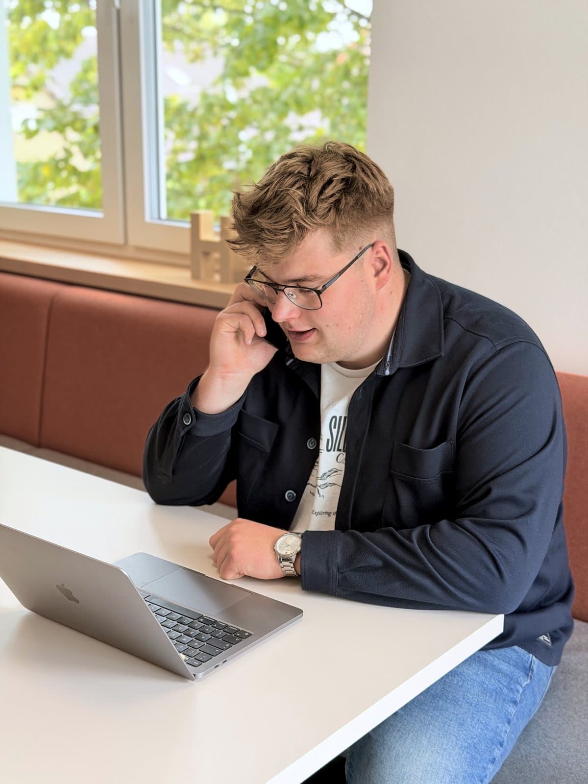 Paul Budde am Telefon, den Laptop vor sich.