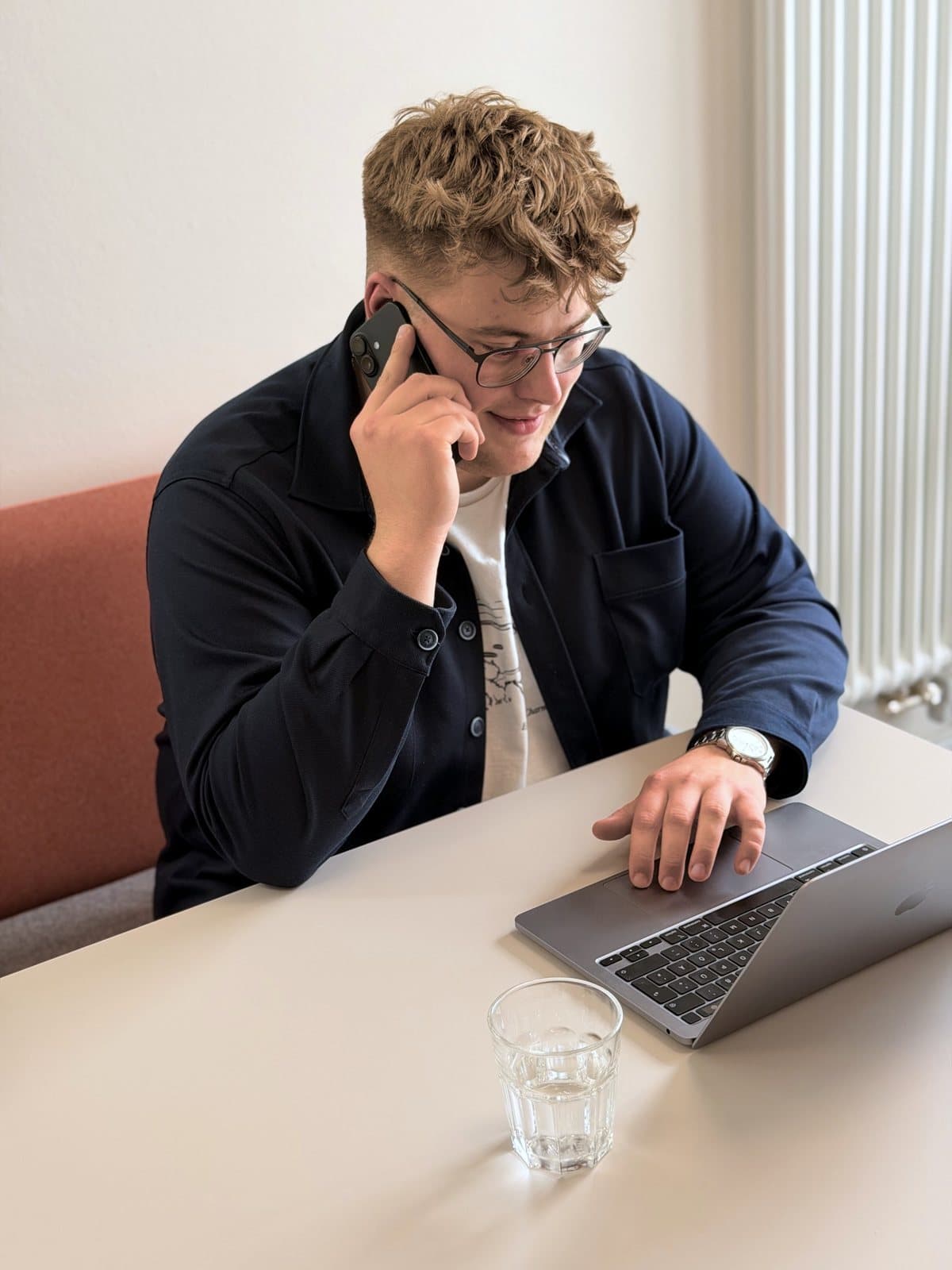 Paul Budde am Telefon, die freie Hand auf dem Laptop, im Hintergrund eine helle Wand.