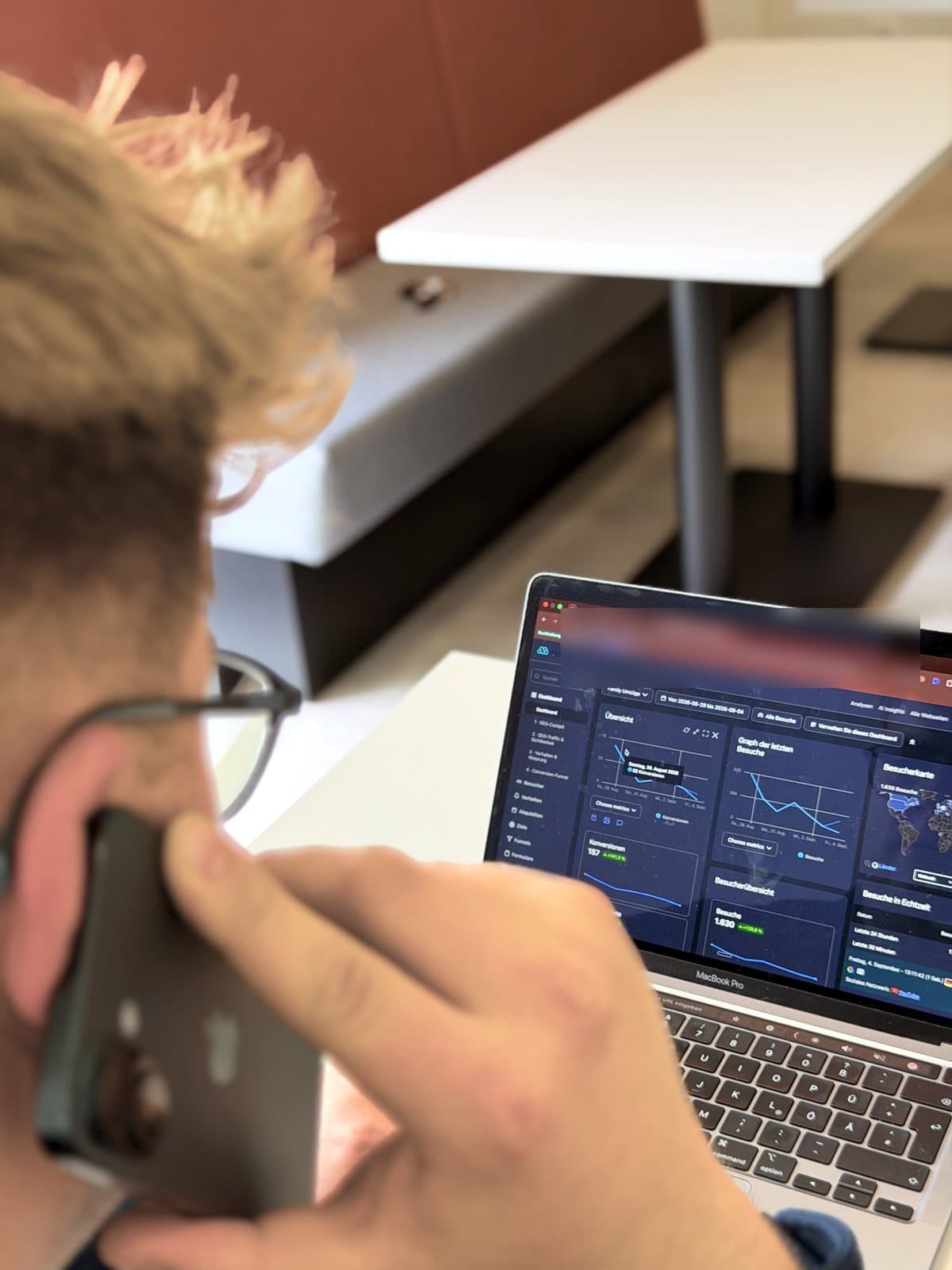 Paul Budde telefoniert, vor ihm auf dem Laptop das Besucher-Dashboard eines Kundenkontos mit den Zahlen einer Woche.